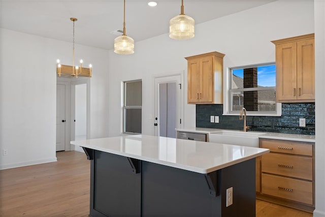 kitchen featuring a kitchen island, a sink, light wood-style floors, light countertops, and backsplash