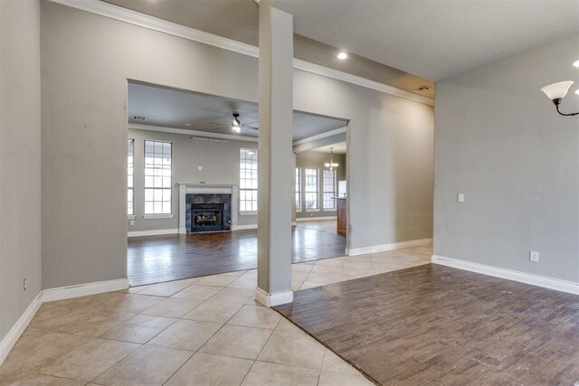 unfurnished living room with light tile patterned floors, crown molding, ceiling fan with notable chandelier, and a high end fireplace