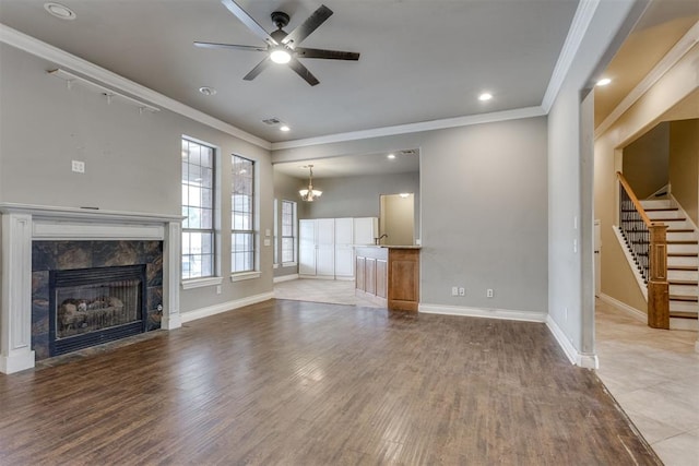 unfurnished living room featuring ornamental molding, a high end fireplace, ceiling fan with notable chandelier, and light hardwood / wood-style flooring