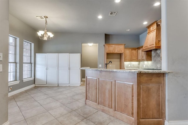 kitchen with tasteful backsplash, hanging light fixtures, kitchen peninsula, a notable chandelier, and light stone countertops