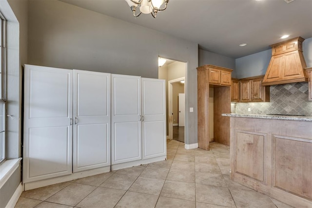 kitchen featuring premium range hood, light brown cabinetry, backsplash, light tile patterned floors, and an inviting chandelier