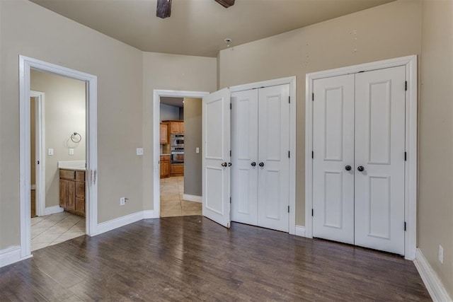 unfurnished bedroom with multiple closets, ensuite bath, and wood-type flooring