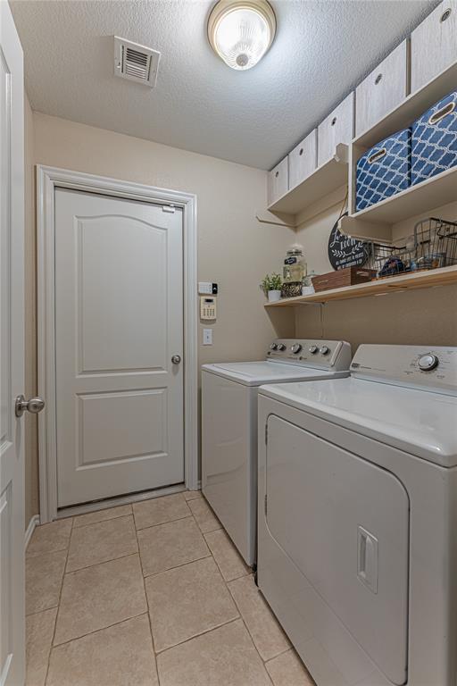 washroom with light tile patterned floors, washing machine and clothes dryer, and a textured ceiling