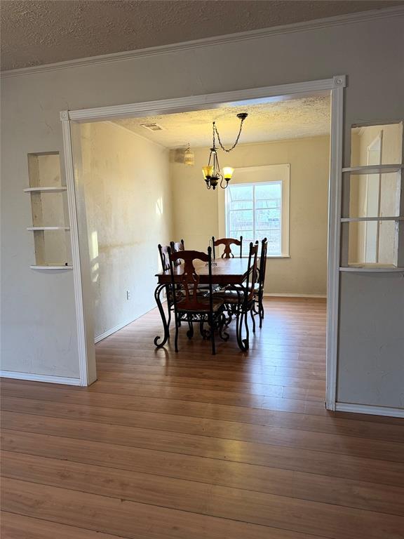 dining room featuring hardwood / wood-style flooring, ornamental molding, a textured ceiling, and a notable chandelier