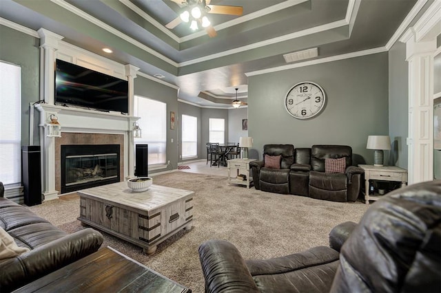 living room with a tiled fireplace, ornamental molding, ceiling fan, a raised ceiling, and light carpet