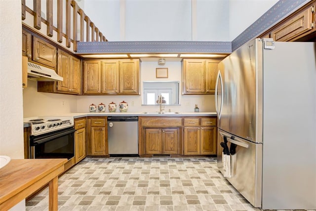 kitchen featuring appliances with stainless steel finishes, brown cabinets, light countertops, under cabinet range hood, and a sink