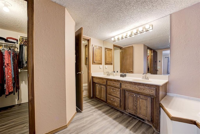 full bathroom featuring double vanity, a spacious closet, a sink, a textured ceiling, and wood finished floors