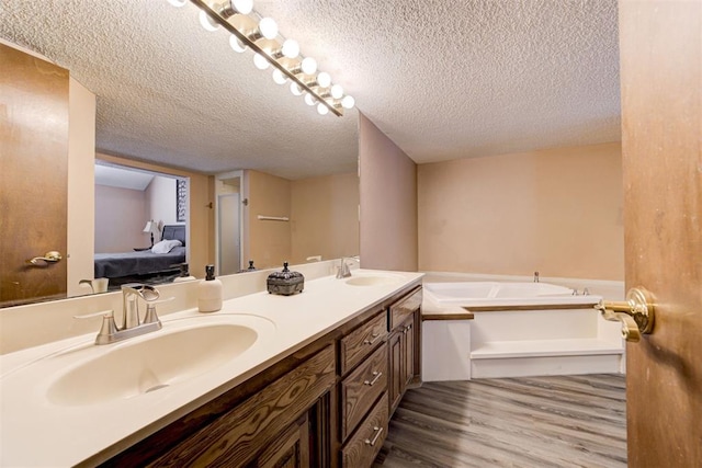 ensuite bathroom featuring double vanity, ensuite bath, a sink, and wood finished floors