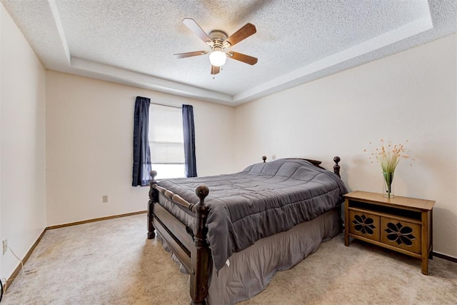 bedroom featuring a textured ceiling, a tray ceiling, baseboards, and light colored carpet