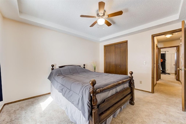 bedroom with a closet, a raised ceiling, light colored carpet, and a textured ceiling