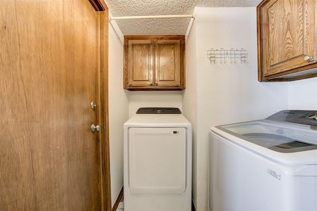 laundry area featuring a textured ceiling, washing machine and clothes dryer, and cabinet space