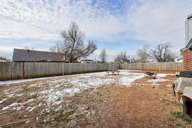 snowy yard with an outdoor fire pit and a fenced backyard