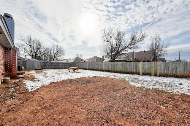 yard layered in snow featuring a shed, a fenced backyard, and an outdoor structure