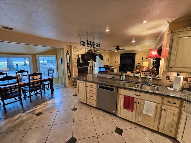 kitchen featuring light brown cabinetry, sink, stainless steel dishwasher, and dark stone counters