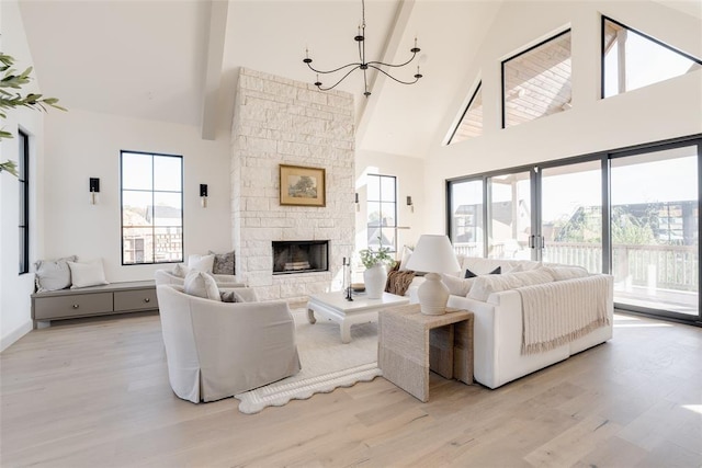 living room with a stone fireplace, an inviting chandelier, high vaulted ceiling, and light hardwood / wood-style flooring