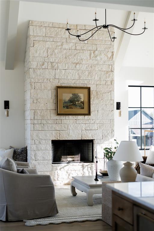 living room with a towering ceiling, hardwood / wood-style floors, an inviting chandelier, a fireplace, and beam ceiling