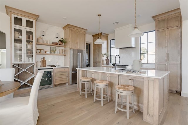 kitchen featuring pendant lighting, high end fridge, an island with sink, and wine cooler