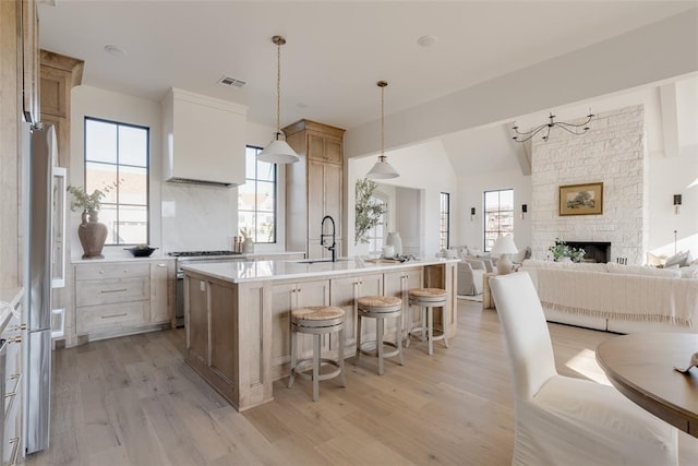 kitchen featuring appliances with stainless steel finishes, a kitchen island with sink, light hardwood / wood-style floors, and decorative light fixtures