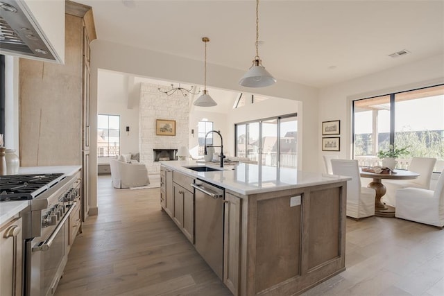 kitchen with appliances with stainless steel finishes, a fireplace, an island with sink, sink, and hanging light fixtures