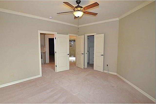 unfurnished bedroom with ceiling fan, ornamental molding, light carpet, a walk in closet, and a closet