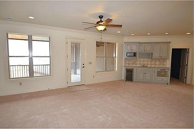 kitchen featuring crown molding, gray cabinets, stainless steel microwave, light carpet, and beverage cooler