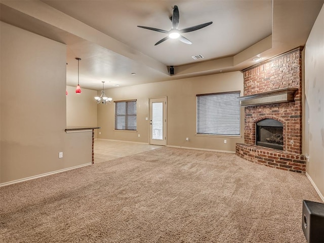 unfurnished living room featuring a raised ceiling, ceiling fan with notable chandelier, a brick fireplace, and light carpet