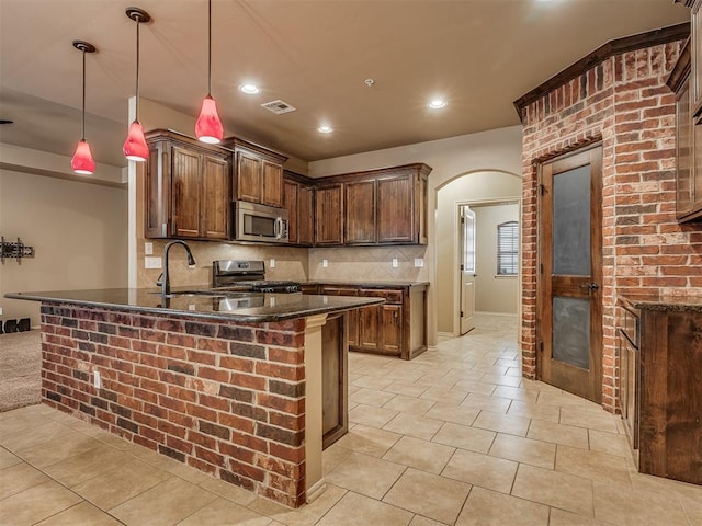 kitchen featuring appliances with stainless steel finishes, hanging light fixtures, backsplash, kitchen peninsula, and dark stone counters