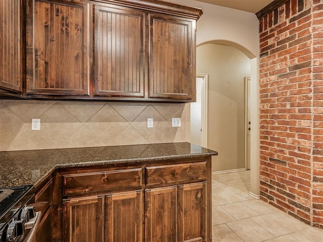 kitchen featuring dark stone countertops, light tile patterned floors, range with electric cooktop, brick wall, and backsplash