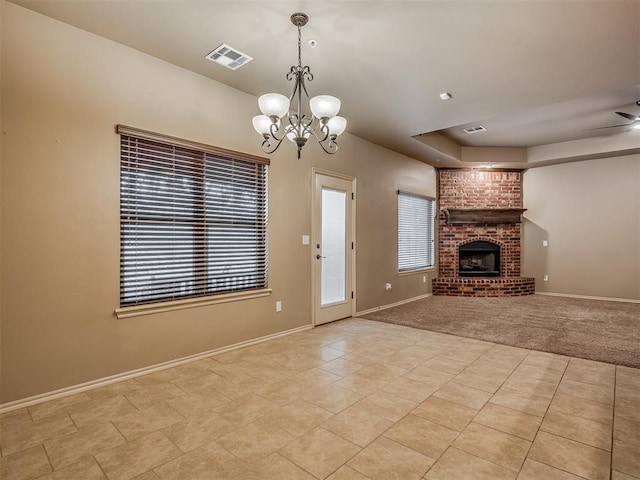 unfurnished living room with ceiling fan with notable chandelier, a fireplace, light tile patterned floors, a tray ceiling, and plenty of natural light