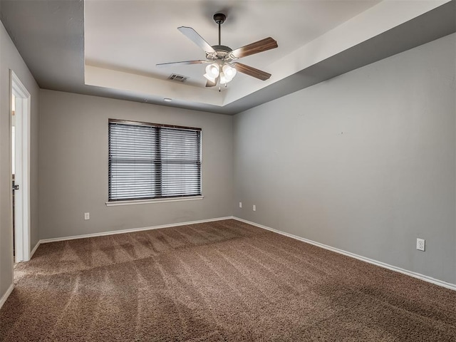 carpeted empty room with a raised ceiling and ceiling fan