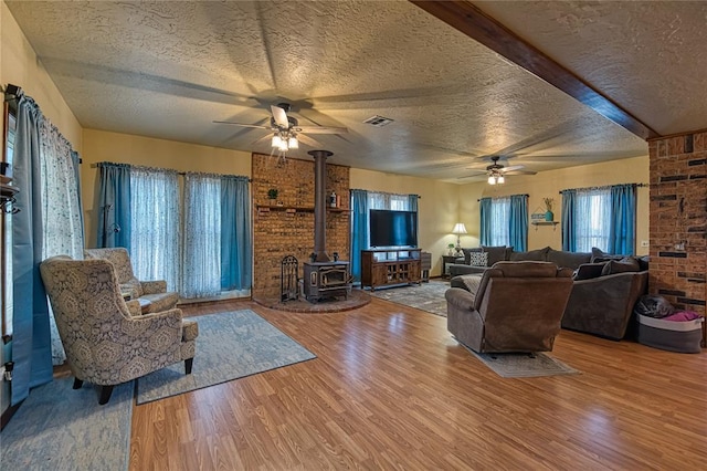 living room featuring hardwood / wood-style flooring, ceiling fan, a textured ceiling, and a wood stove