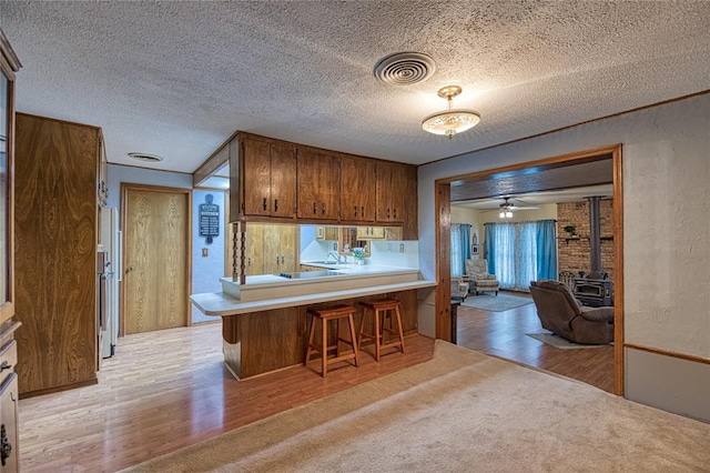 kitchen with a breakfast bar, a textured ceiling, light wood-type flooring, a wood stove, and kitchen peninsula