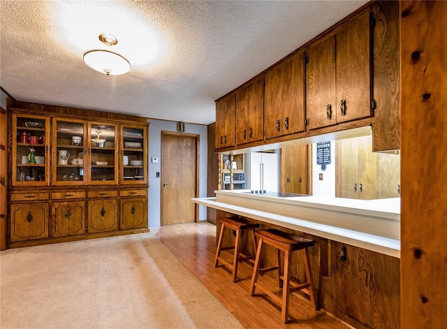 kitchen featuring a textured ceiling, black electric cooktop, high quality fridge, a kitchen breakfast bar, and light hardwood / wood-style floors