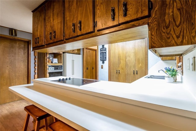 kitchen featuring high end white refrigerator, sink, a breakfast bar area, black electric cooktop, and wall oven