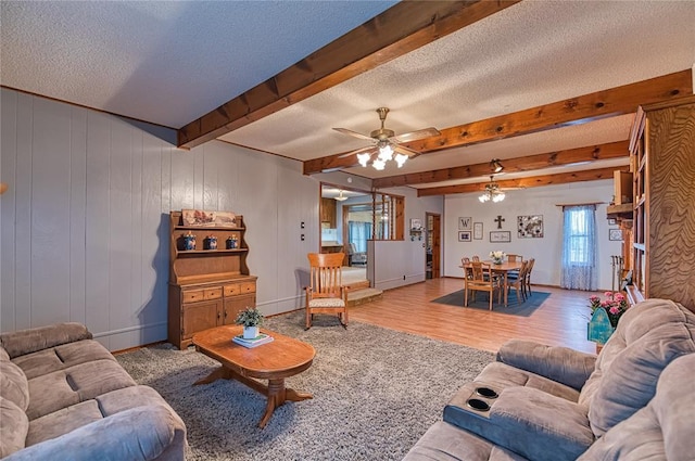 living room with ceiling fan, light wood-type flooring, a textured ceiling, and beam ceiling