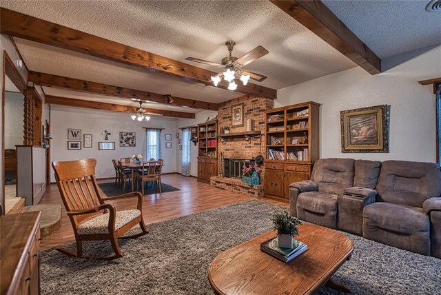 living room featuring wood-type flooring, beam ceiling, a brick fireplace, and a textured ceiling