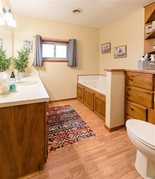 bathroom featuring vanity, a tub to relax in, hardwood / wood-style flooring, and toilet