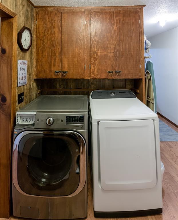 laundry room featuring cabinets, light wood-type flooring, washing machine and clothes dryer, and a textured ceiling