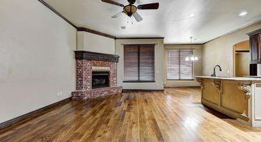 living room featuring hardwood / wood-style flooring, crown molding, ceiling fan with notable chandelier, and a brick fireplace