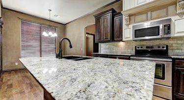 kitchen featuring sink, stainless steel appliances, dark brown cabinetry, light stone counters, and an island with sink