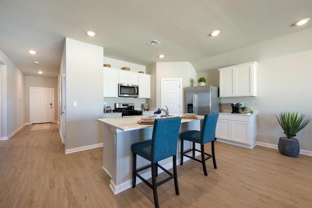 kitchen with a breakfast bar, visible vents, light countertops, appliances with stainless steel finishes, and a center island with sink