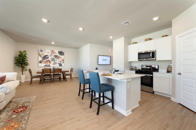 kitchen with visible vents, white cabinets, an island with sink, stainless steel appliances, and light countertops