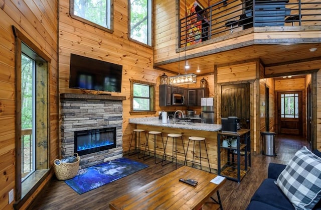 living room featuring a stone fireplace, sink, dark hardwood / wood-style floors, wooden walls, and a high ceiling