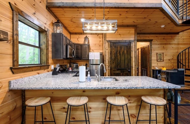 kitchen featuring light stone counters, a peninsula, wood walls, wood ceiling, and appliances with stainless steel finishes