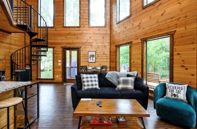 living area with dark wood-style flooring, wooden walls, a towering ceiling, and stairs