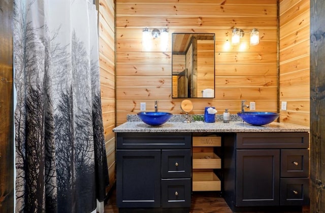 bathroom with double vanity, curtained shower, wood walls, and a sink