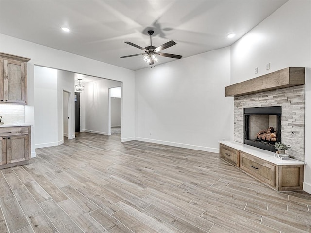 unfurnished living room with a stone fireplace, ceiling fan, and light wood-type flooring