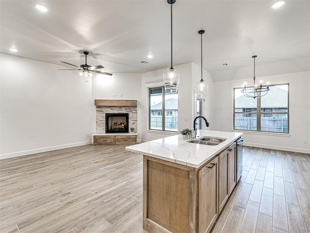 kitchen featuring a fireplace, decorative light fixtures, an island with sink, sink, and light stone countertops