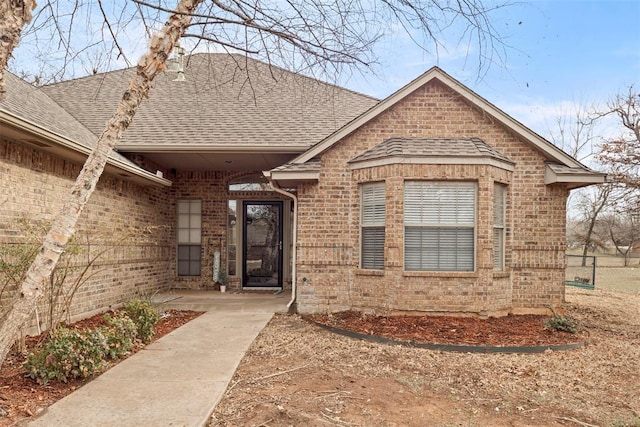 doorway to property featuring brick siding and roof with shingles