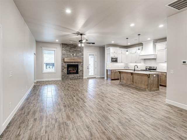 unfurnished living room with sink, a fireplace, light hardwood / wood-style floors, and ceiling fan